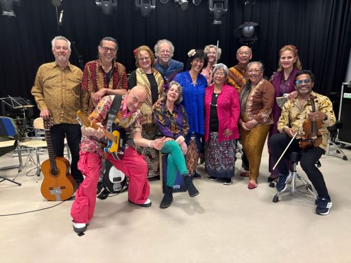 Een kleurrijke groep muzikanten in traditionele kleding, staand en zittend in een zaal.